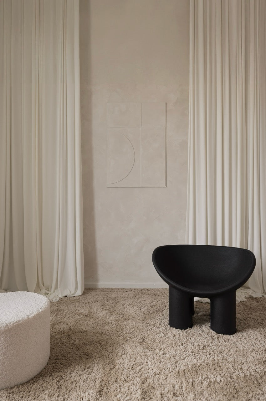 Minimalistyczna aranżacja studia fotograficznego Silky Studio z czarnym fotelem, białą zasłoną i kremową ścianą dekoracyjną.