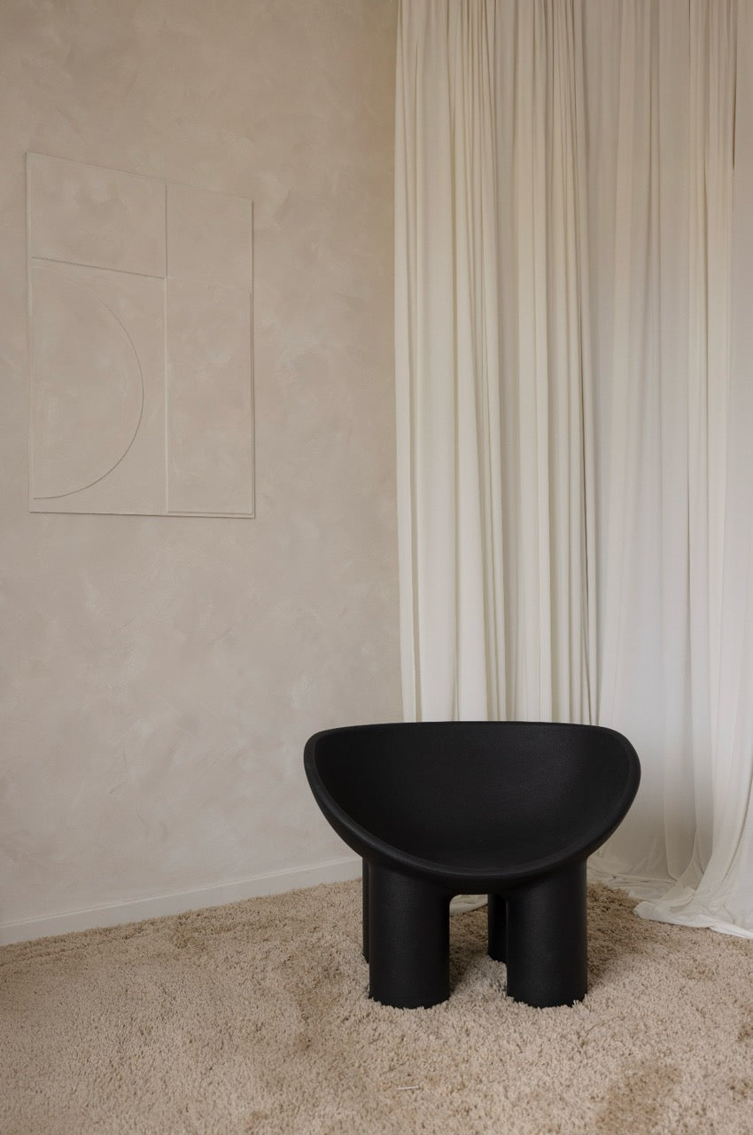 Designerski czarny fotel w Silky Studio na tle jasnych zasłon i kremowej ściany – minimalistyczna przestrzeń do sesji.